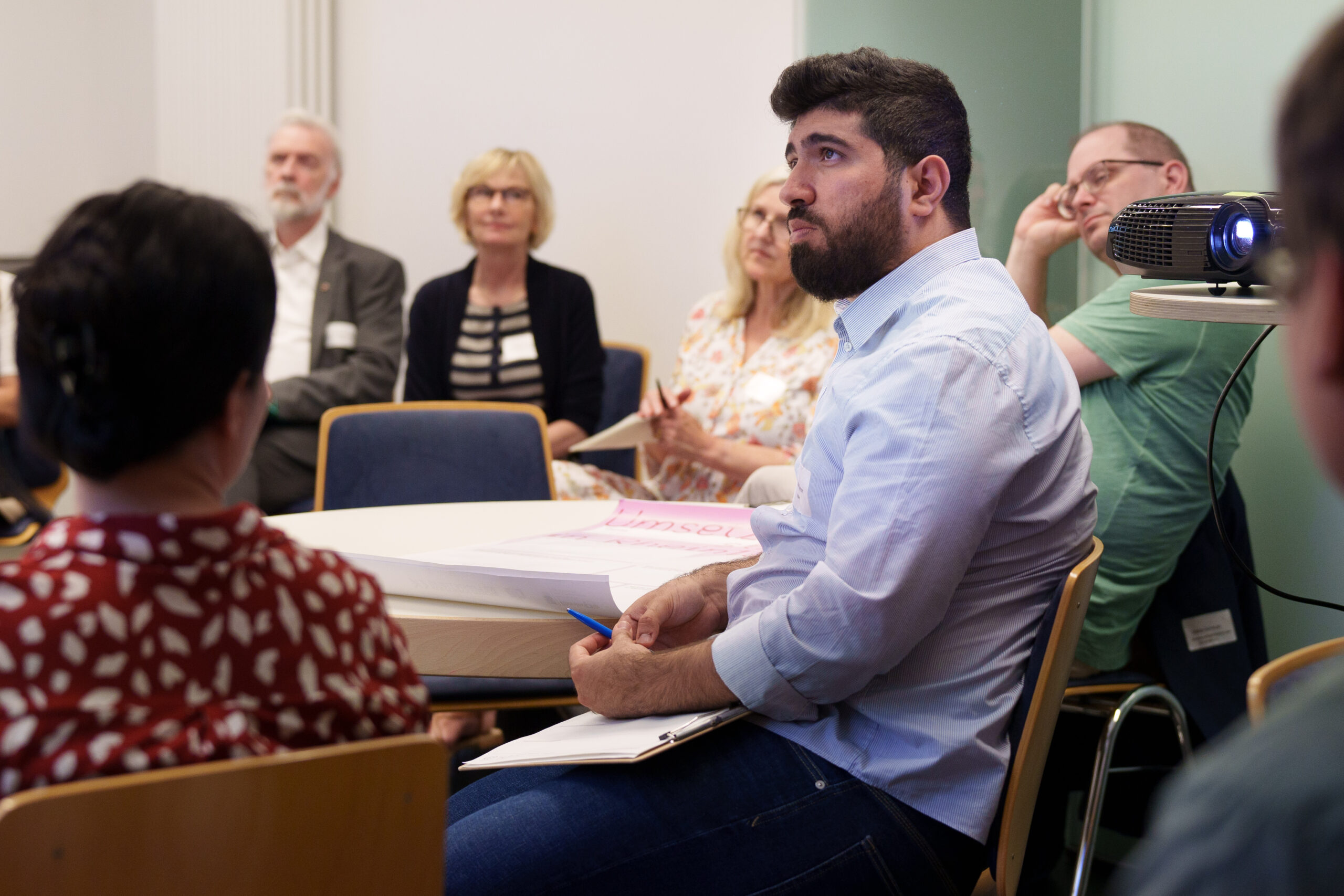 Diskussionsrunde des vierten Themenforums. Die Teilnehmenden blicken sehr konzentriert auf eine Präsentation. Im Hintergrund sind der Kulturstaatssekretär Prof. Dr. Jürgen Hardeck und Dorothee Rhiemeyer vom MFFKI zu sehen.