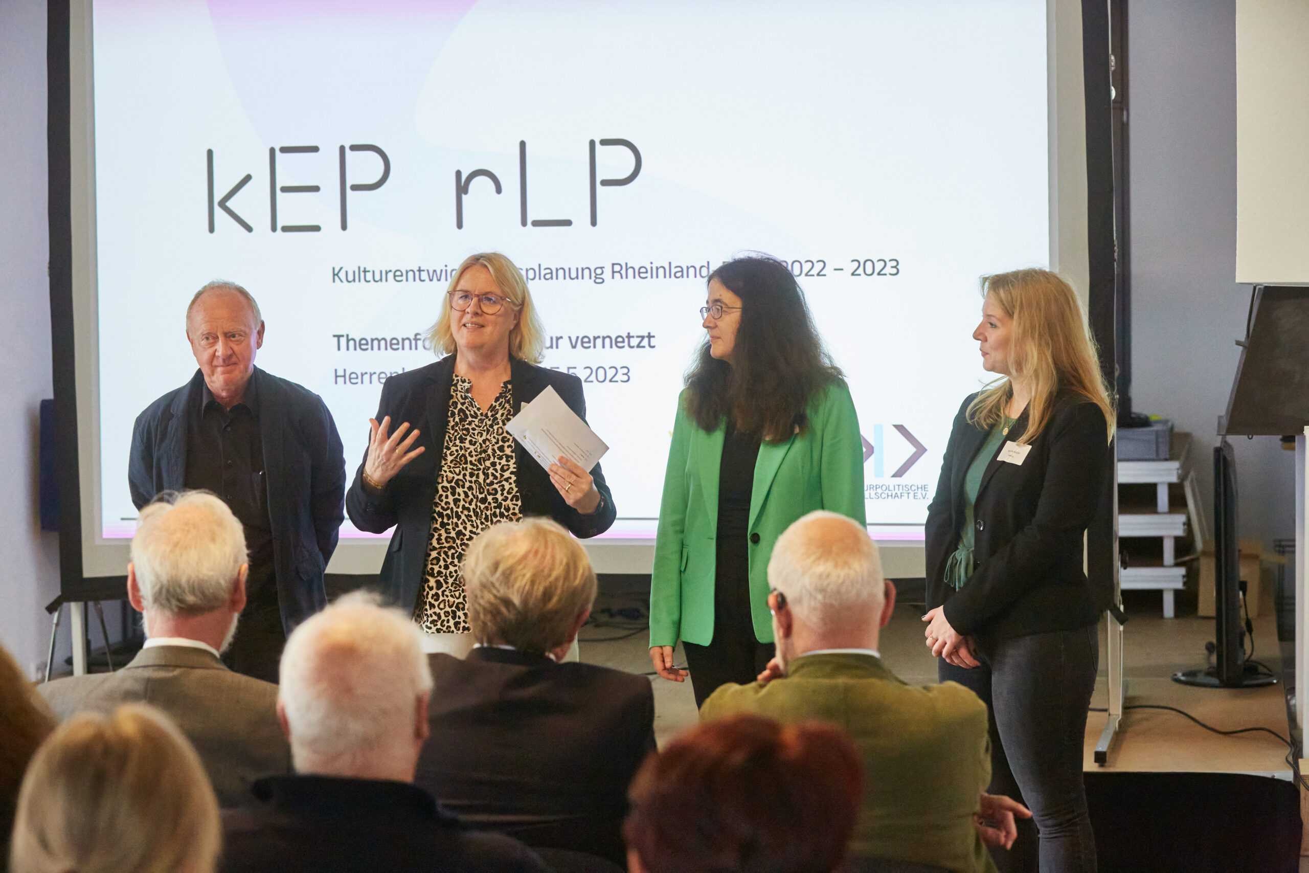 Das Team der Prozessbegleitung für die Kulturentwicklungsplanung in Rheinland-Pfalz. Kurt Eichler, Anke von Heyl, Ulrike Blumenreich und Tamina Müller. Im Hintergrund sieht man eine Präsentation mit der Überschrift KEP rlp