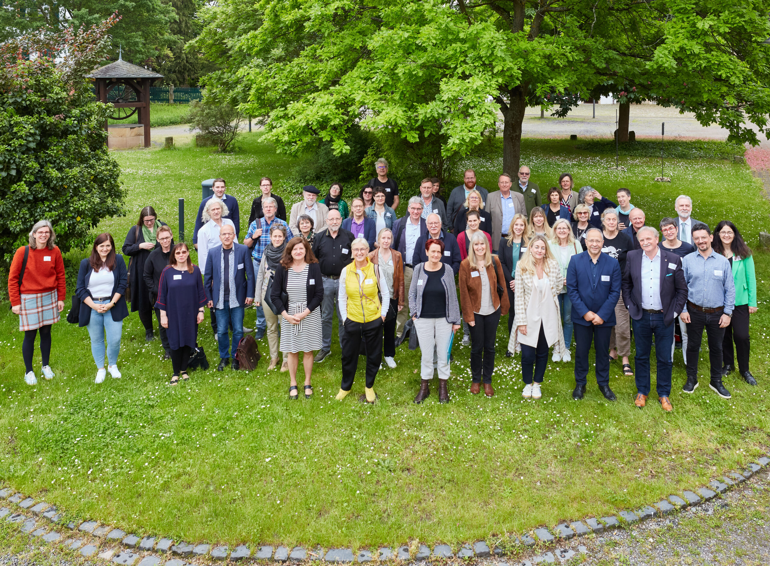 Gruppenbild mit allen Teilnehmenden des zweiten Themenforums der Kulturentwicklungsplanung in Rheinland-Pfalz, bei dem es um Vernetzung ging. Das Foto ist von oben aufgenommen. Die Teilnehmenden stehen auf einem Rasenstück. Im Hintergrund sieht man Bäume