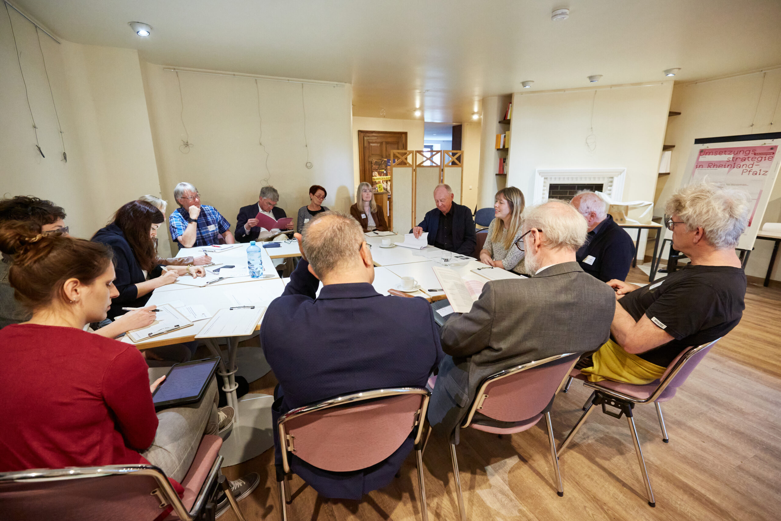 Blick in eine Diskussionsrunde beim zweiten Themenforum. Eine Gruppe von 15 Personen diskutiert miteinander. Rechts steht eine Flipchart